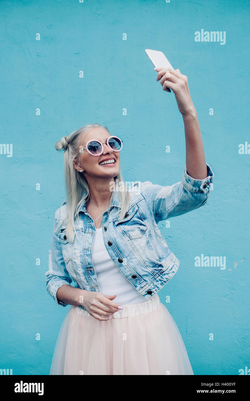 Felice di moda giovane donna parlando selfie contro la parete blu Foto Stock