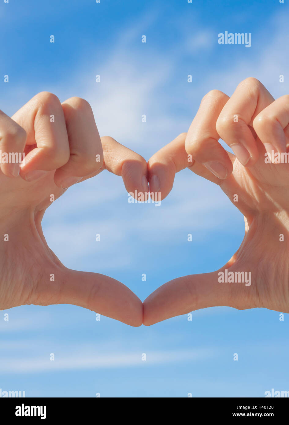 Forma di cuore formato da mani sul cielo blu sullo sfondo Foto Stock