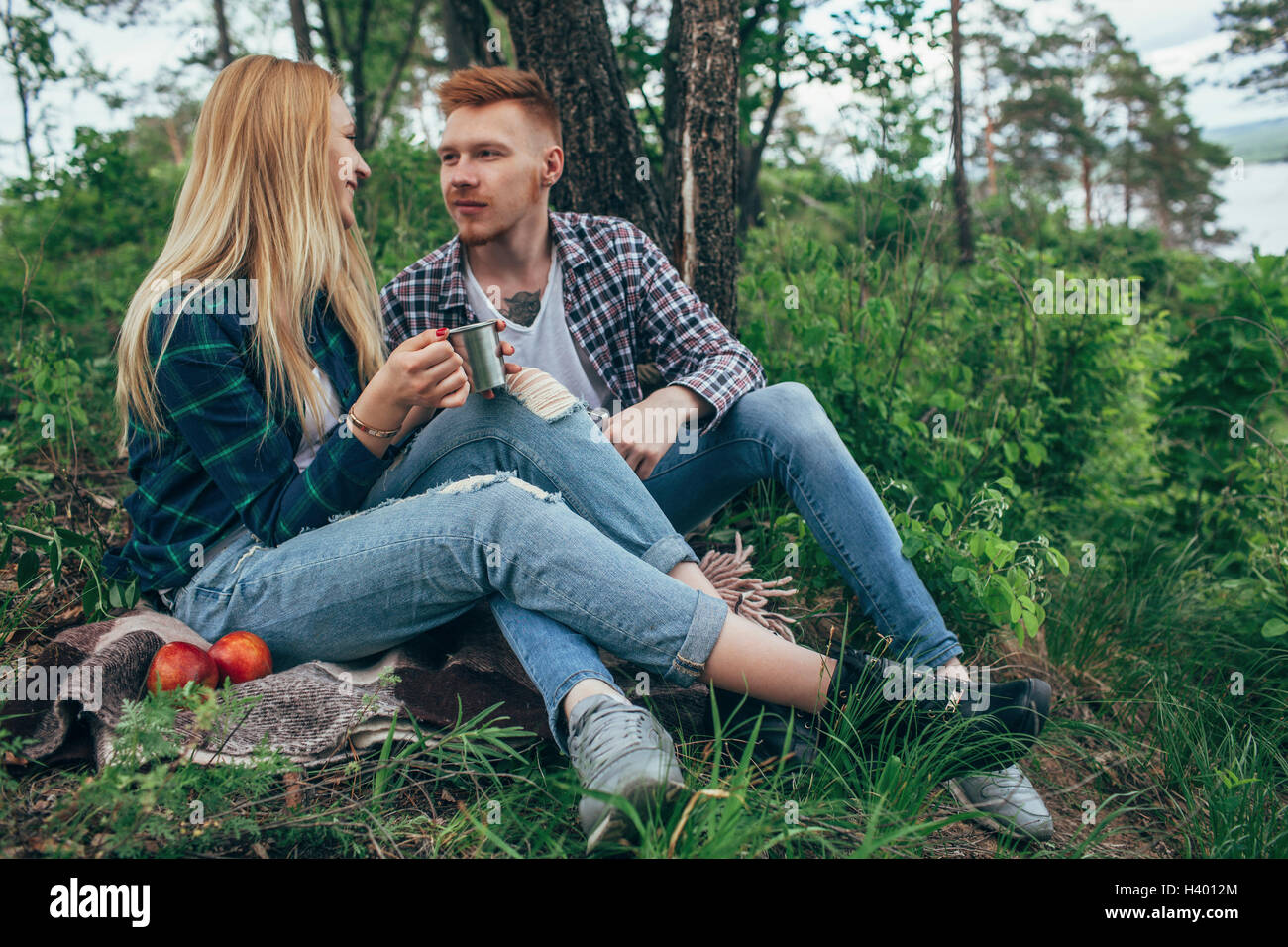 Uomo che guarda ragazza tenendo la tazza durante il riposo sotto albero nella foresta Foto Stock
