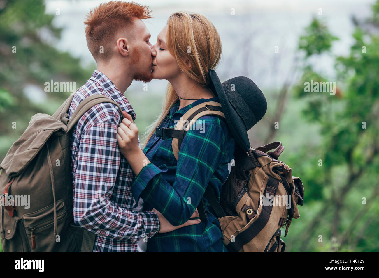 Amare giovane indossando zaini kissing mentre si sta in piedi in foresta Foto Stock