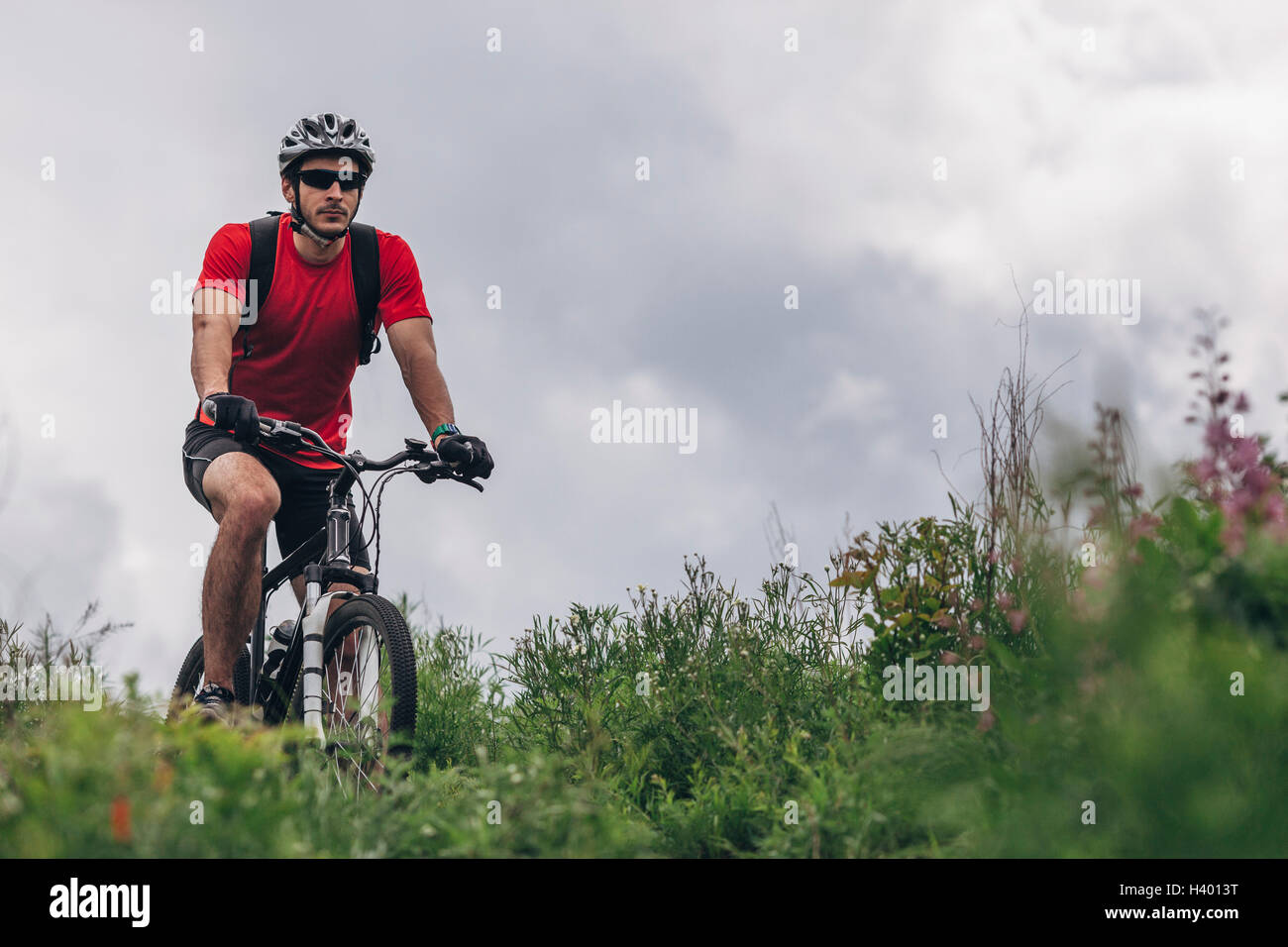 Determinato uomo equitazione mountain bike contro il cielo nuvoloso Foto Stock