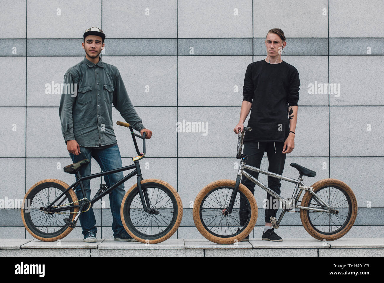 Certi amici in piedi con le biciclette sul marciapiede contro la parete Foto Stock