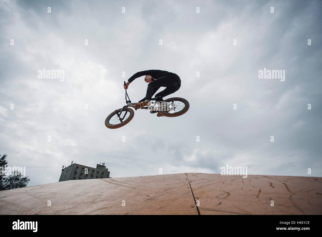 Basso angolo vista di adolescente eseguendo acrobazie durante la BMX ciclismo contro il cielo nuvoloso Foto Stock