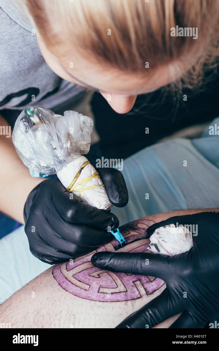 Close-up di artista il tatuaggio sul design dell'uomo in gamba studio Foto Stock