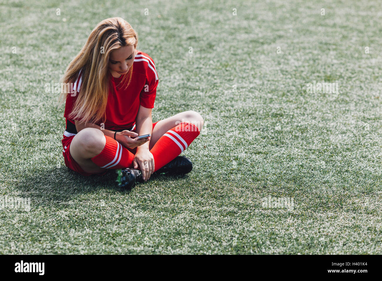 Giocatore di calcio utilizzando smart phone mentre è seduto sul campo Foto Stock
