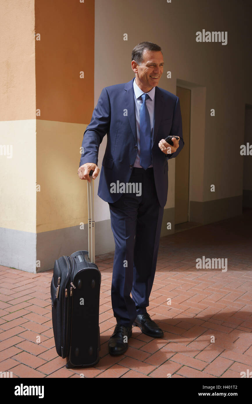 Happy businessman tenendo il telefono cellulare e la valigia mentre si sta in piedi in ufficio Foto Stock