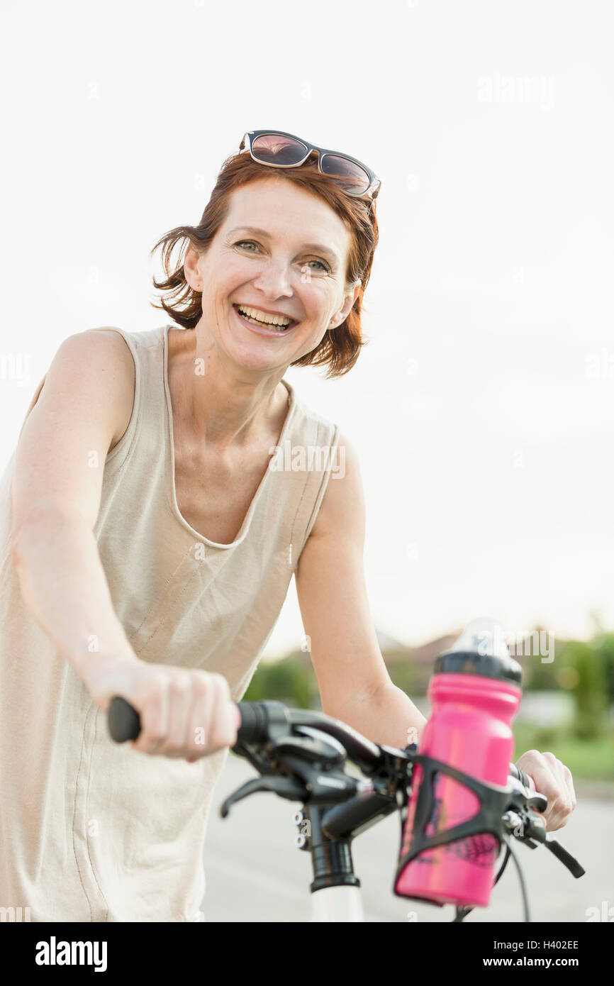 Ritratto di donna sorridente equitazione Bicicletta contro il cielo chiaro Foto Stock