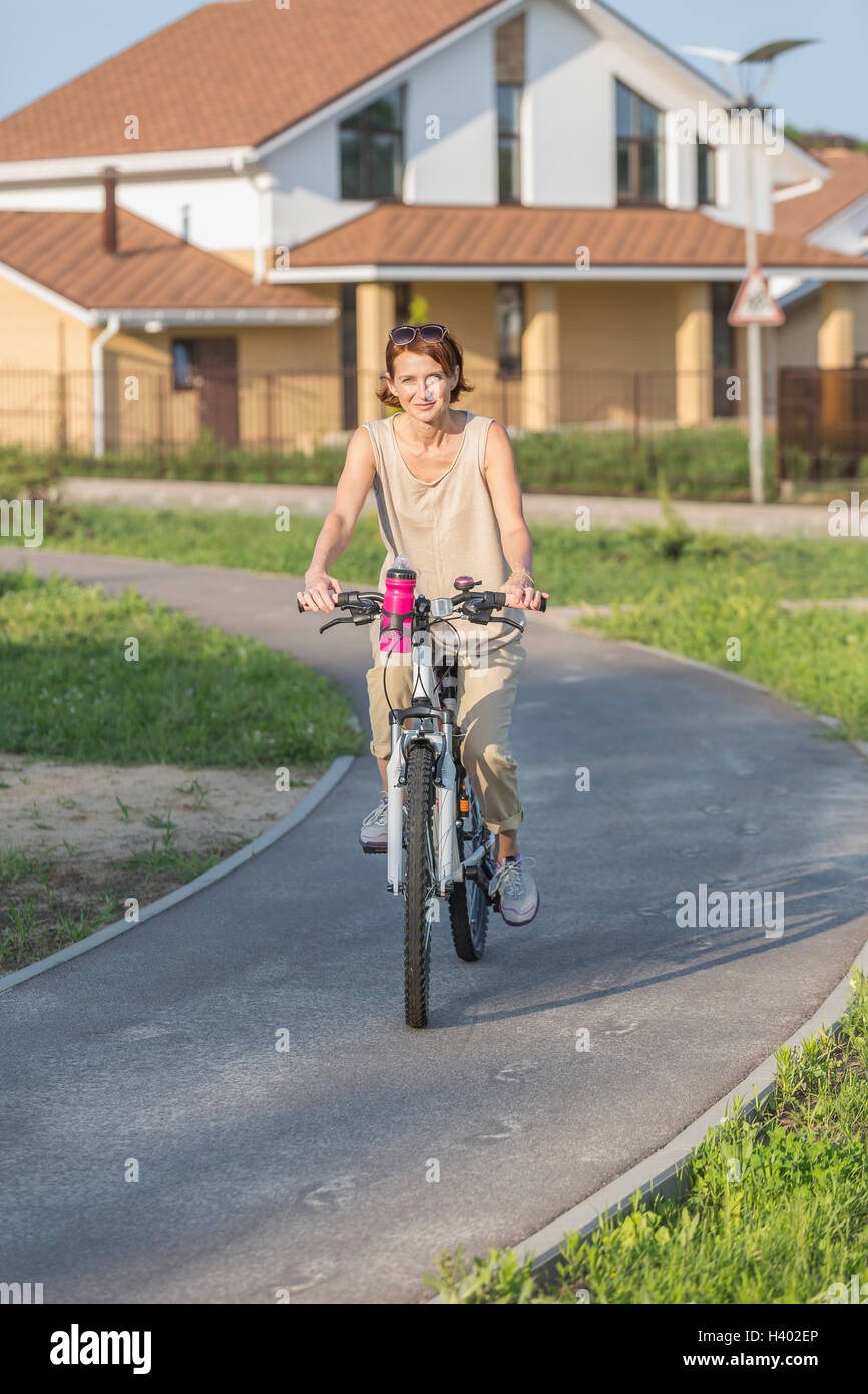 Ritratto di donna Bicicletta Equitazione sulla strada contro la casa Foto Stock