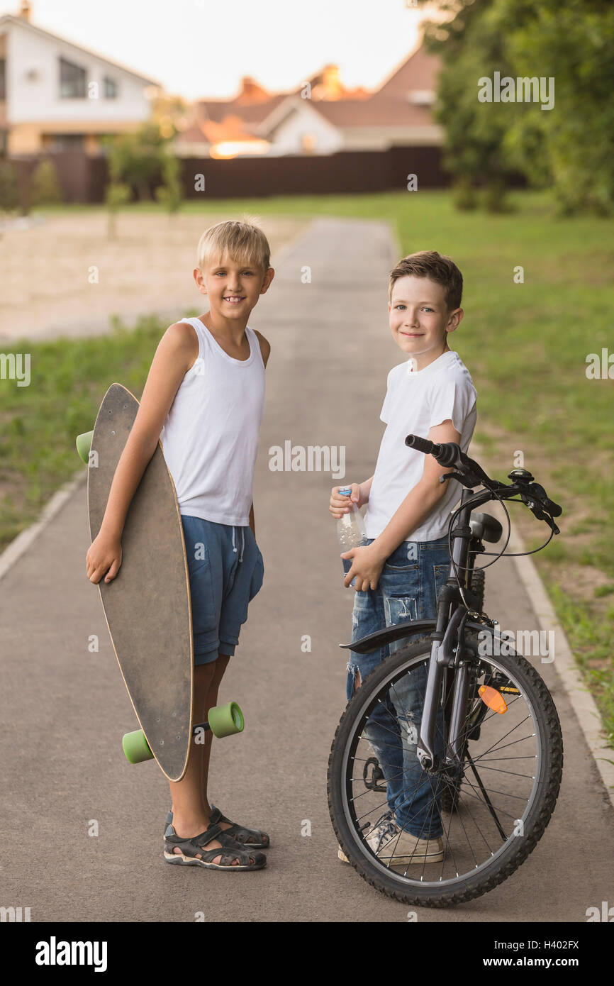 Amici sorridente con lo skateboard e la bicicletta in piedi in posizione di parcheggio Foto Stock