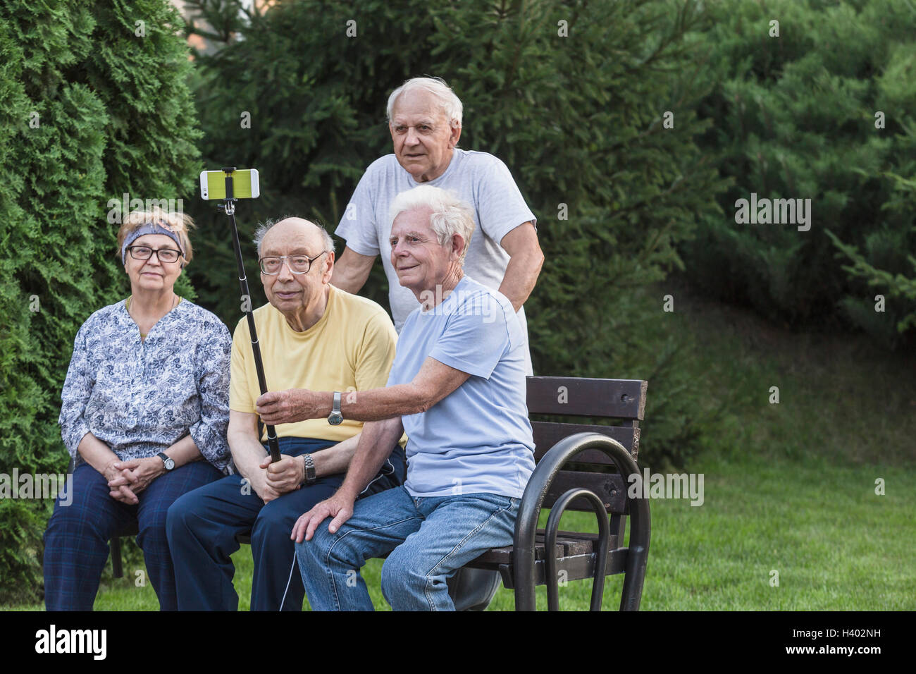 Sorridente senior amici prendendo selfie utilizzando monopiede a una panchina nel parco Foto Stock