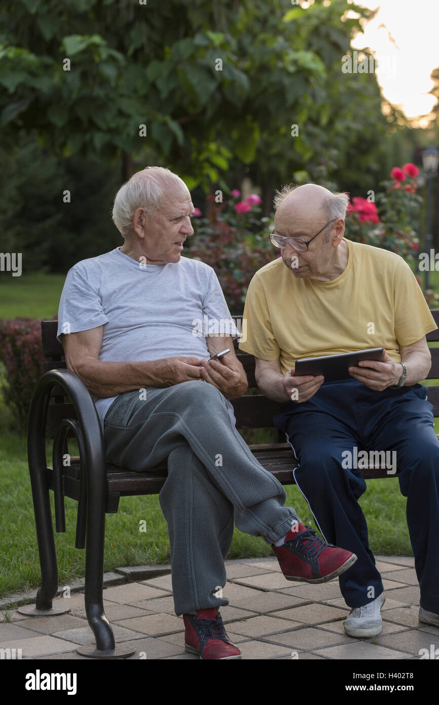 Senior amici utilizzando la tecnologia mentre è seduto in una panchina nel parco Foto Stock