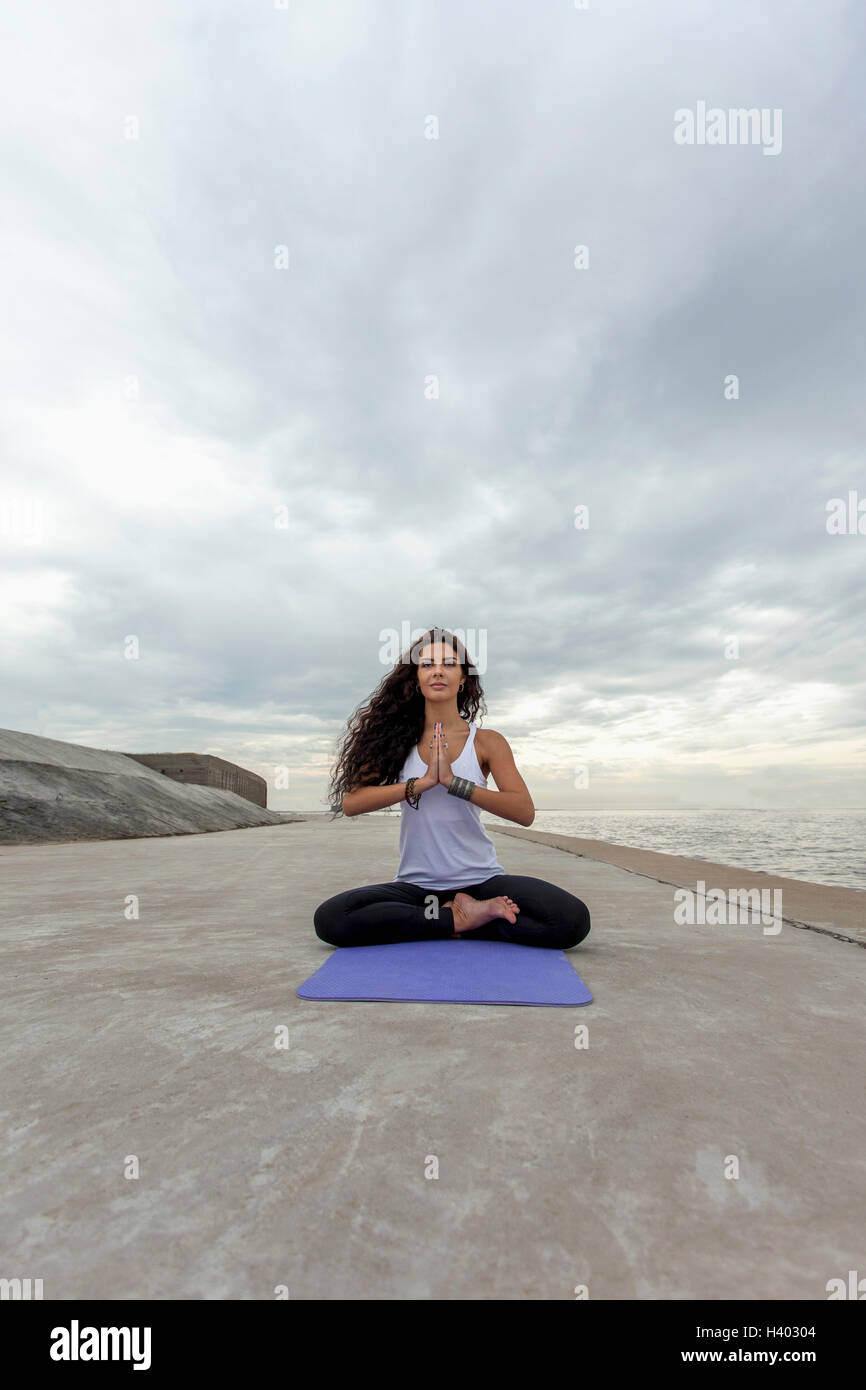Giovane donna a praticare yoga in posizione di preghiera presso la spiaggia contro il cielo nuvoloso Foto Stock