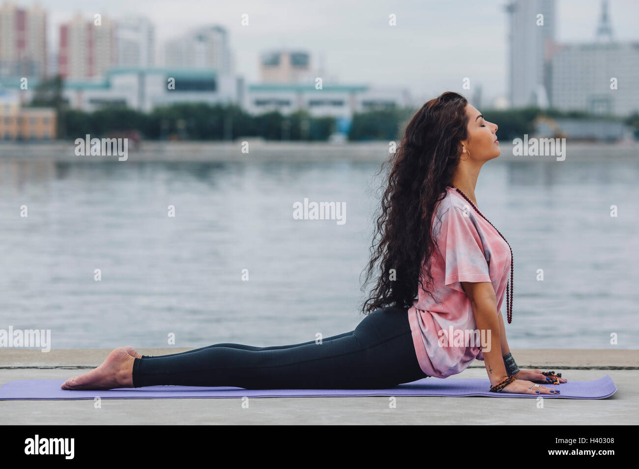 Vista laterale della donna a praticare yoga in cobra pongono dal fiume al city Foto Stock