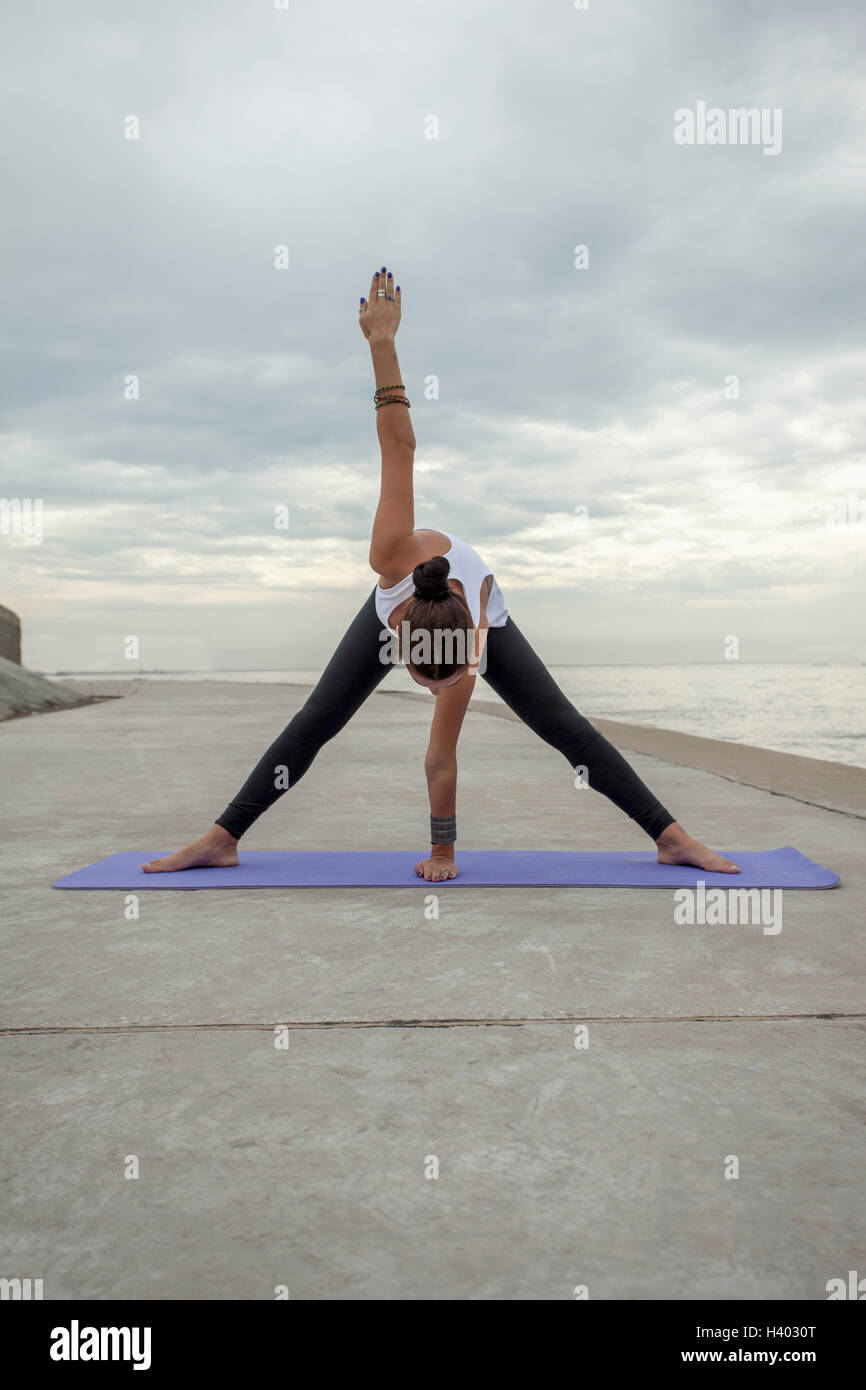 La donna a praticare yoga in spiaggia contro il cielo nuvoloso Foto Stock