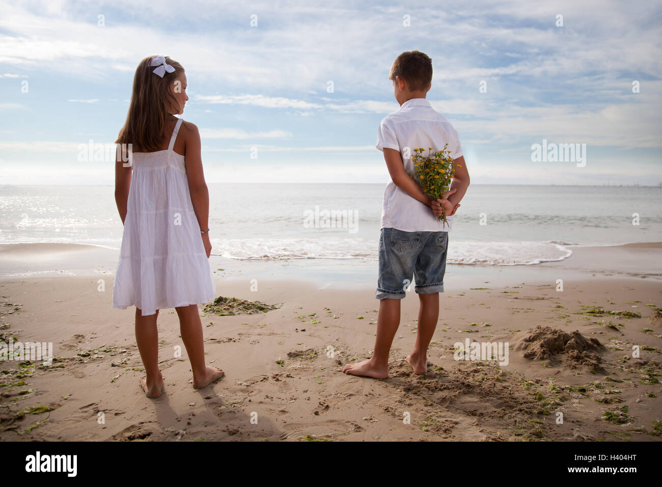 Ragazzo holding fiori alle sue spalle, in piedi accanto alla ragazza sulla spiaggia Foto Stock