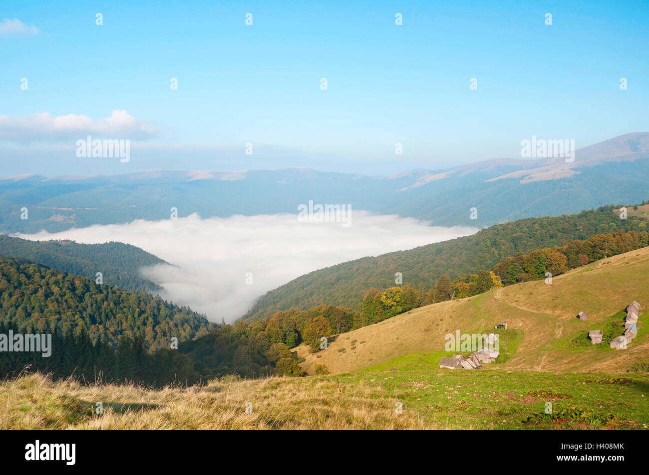 La nebbia paesaggio montano di sunrise nei Carpazi. Vecchia casa in legno in una valle di montagna. Foto Stock