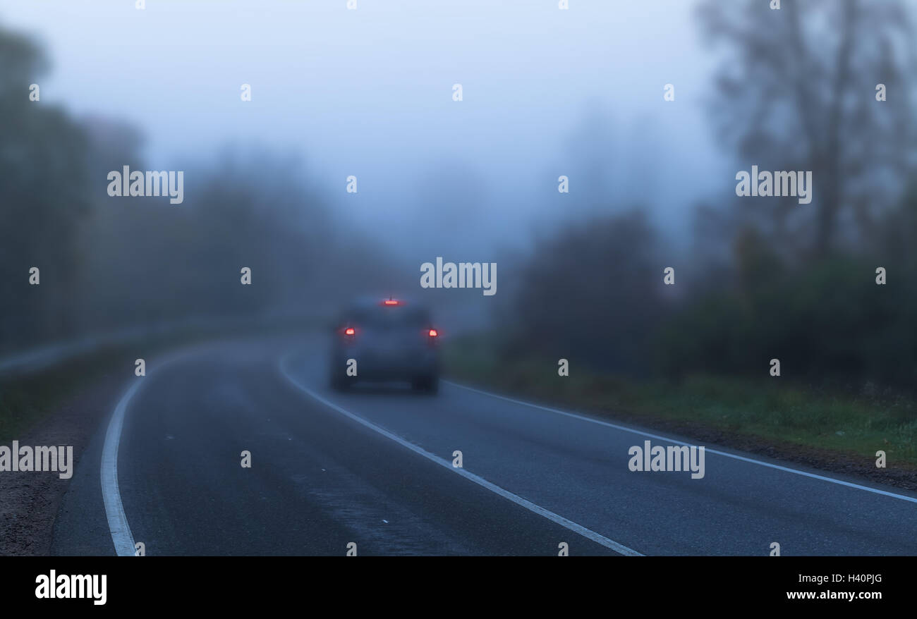 Auto con luci di arresto di colore rosso si accende vuota autostrada rurale in scuro autunno mattinata nebbiosa, tonalità blu del filtro di correzione effetto. D poco profonda Foto Stock