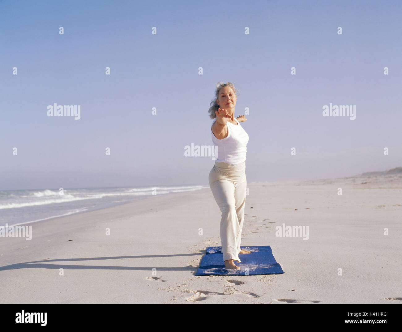 Spiaggia di sabbia, donna, ginnastica pratica migliore età, 50-60 anni, con  i capelli lunghi, grigio-pelose, abbigliamento sportivo, ginnastica,  abbigliamento per il tempo libero in modo comodo, tappetino di ginnastica,  ginnastica, pratica yoga,