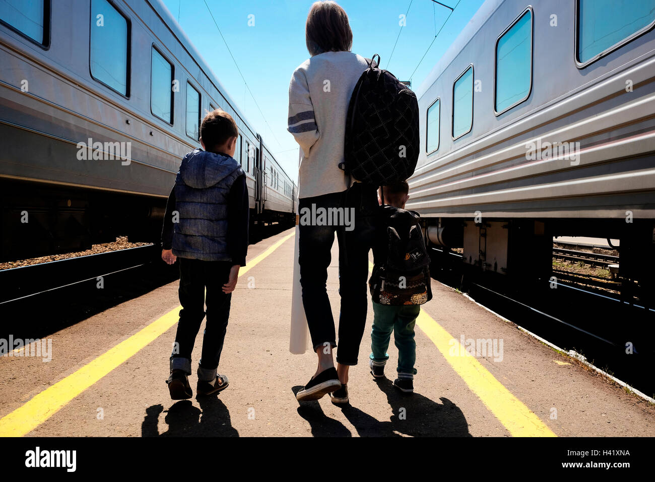 Madre e figli passeggiando tra i treni a stazione ferroviaria Foto Stock
