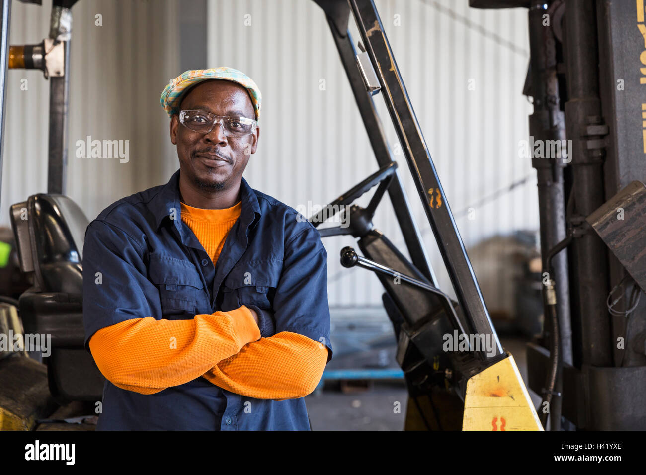 Sorridente lavoratore nero in posa vicino al carrello elevatore a forche in fabbrica Foto Stock