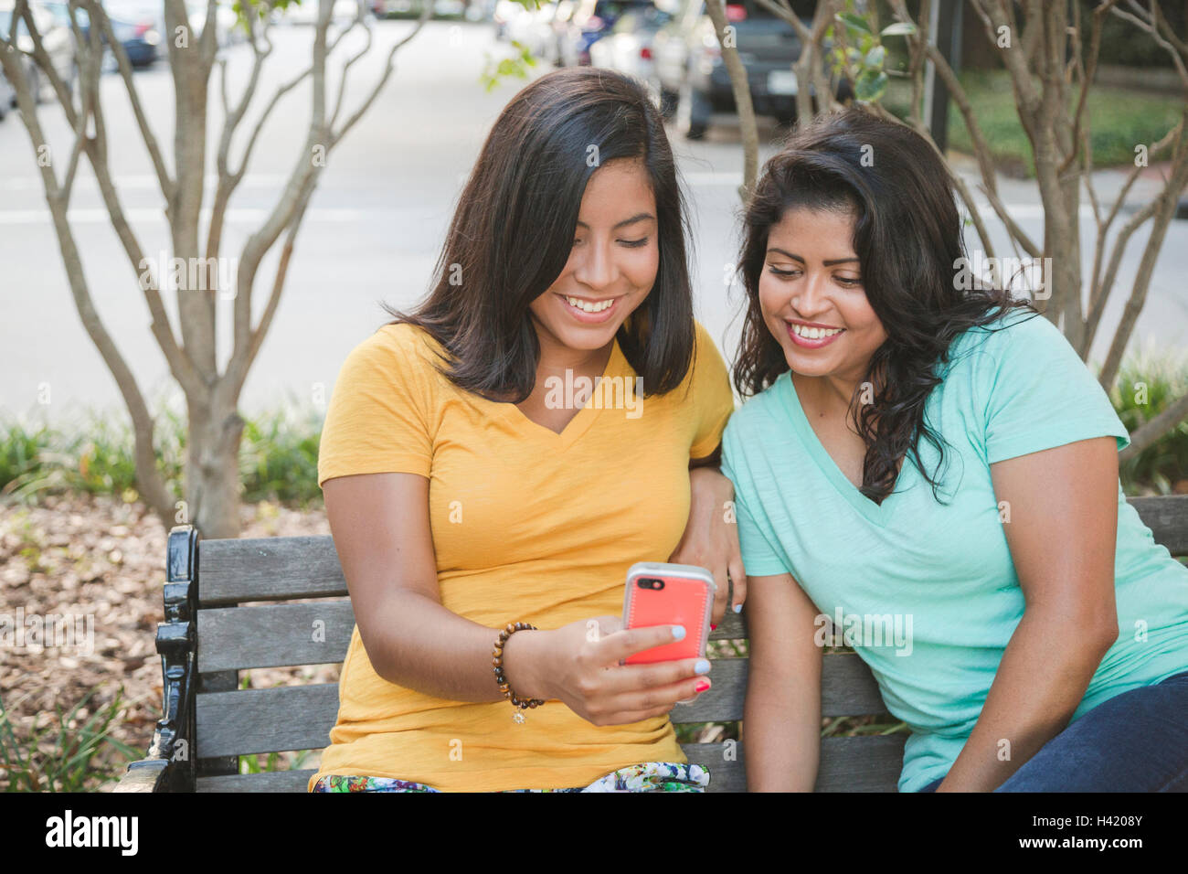 Ispanico madre e figlia tramite telefono cellulare su una panchina nel parco Foto Stock