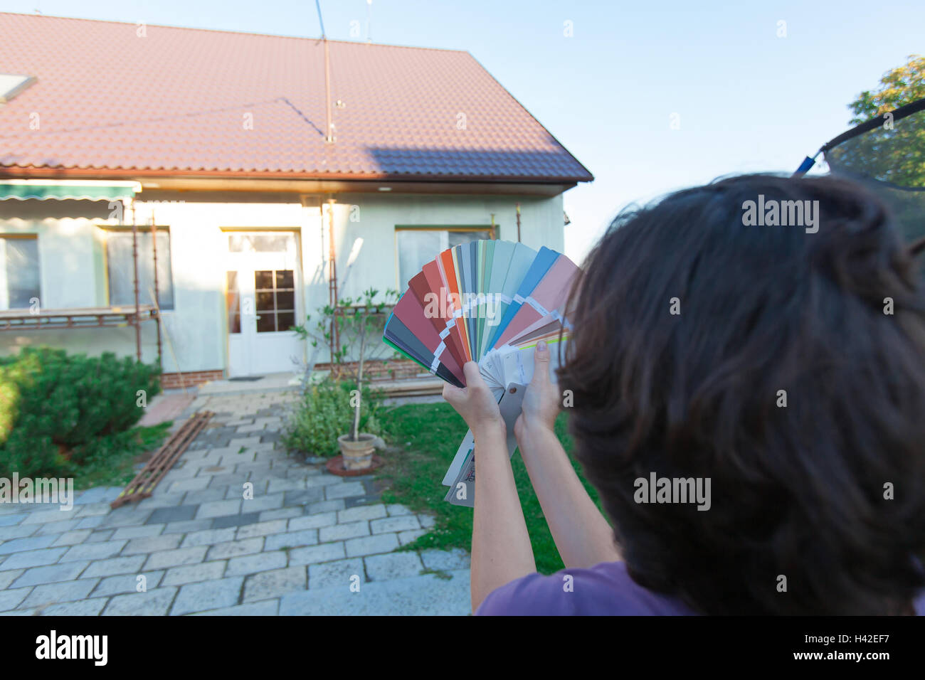 Giovane donna sceglie un nuovo colore per la loro casa. Scegliere i colori per una nuova facciata. (Focus sul campionatore, tutti in primo piano un Foto Stock