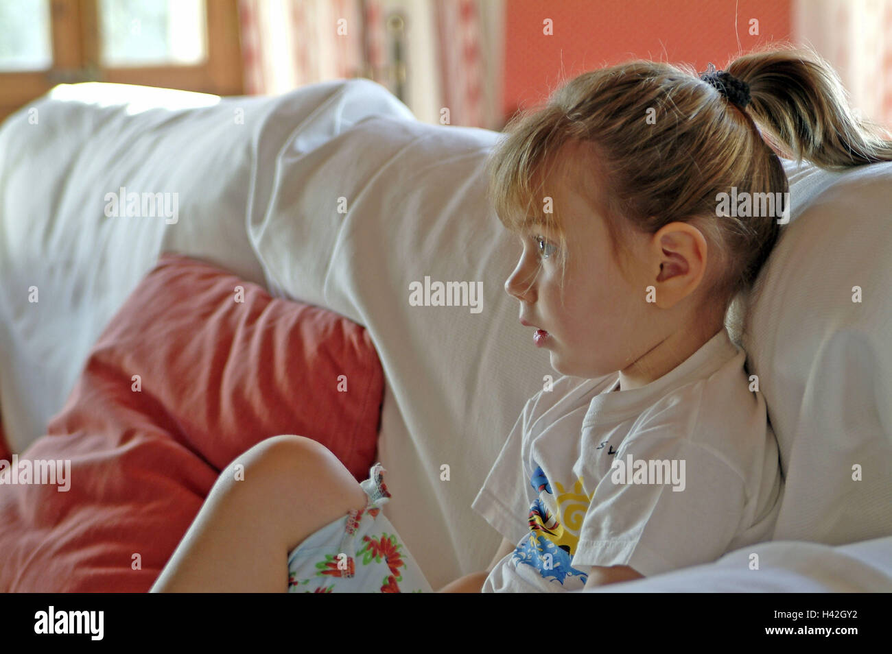 Le ragazze, 5 anni, divano, guarda la televisione, stirata, profilo bambino, infanzia, a casa, tempo libero e coda di cavallo, lo sguardo verso la parte anteriore, alertly, interessante sul lato Foto Stock