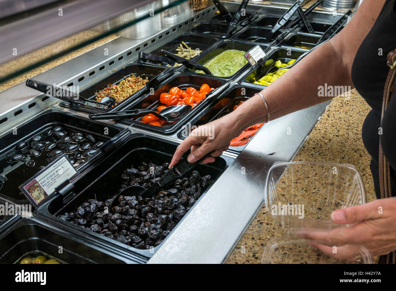 Donna selezionando Dry cured Beldi nero olive da un supermercato self-service di contatore di delicatessen. Foto Stock