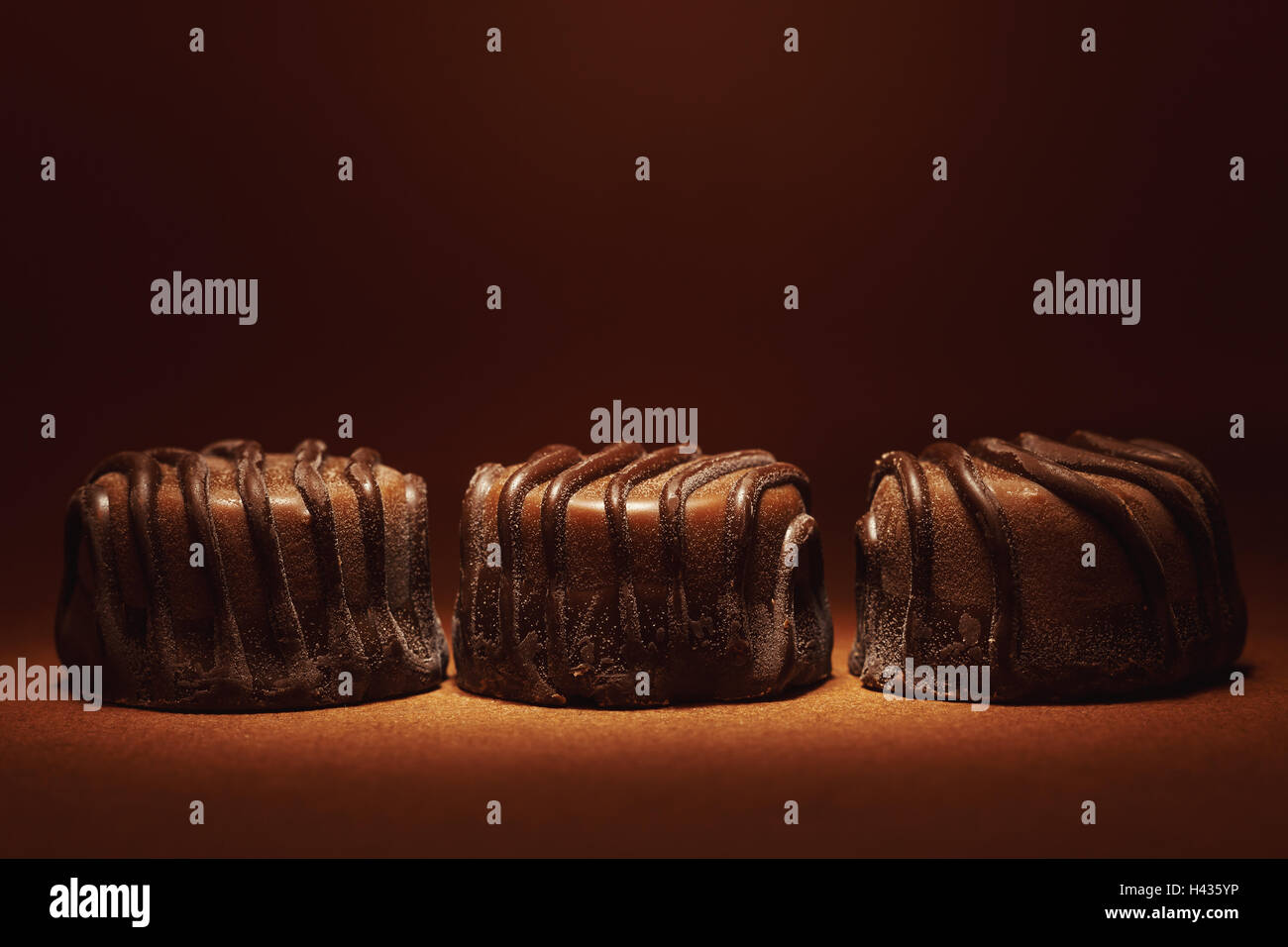 Primo piano vista macro di tre stessi cioccolatini, su sfondo marrone. Foto Stock
