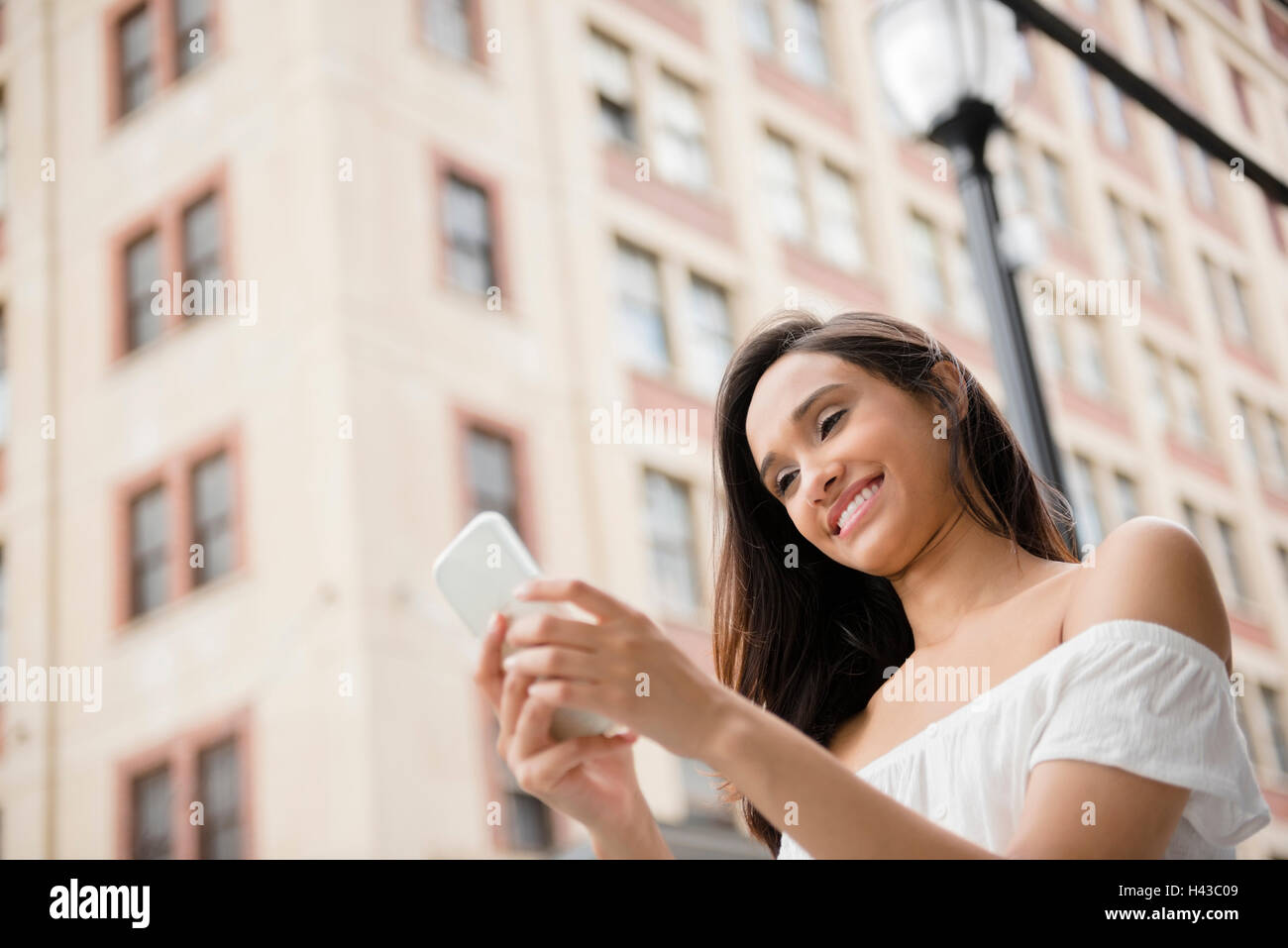 Sorridente razza mista donna sms sul cellulare in città Foto Stock