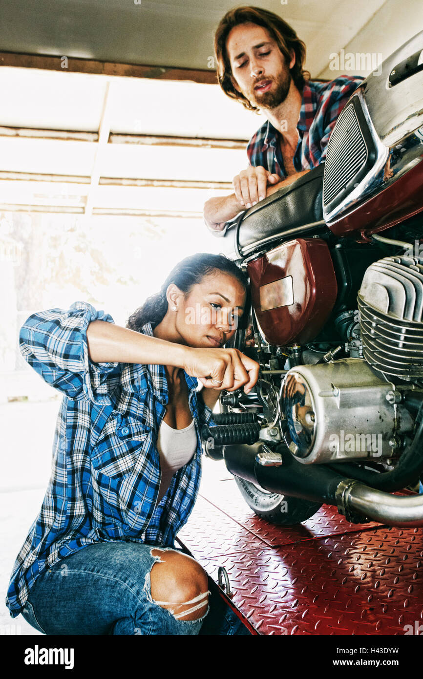 L'uomo guarda la donna la riparazione di moto nel garage Foto Stock