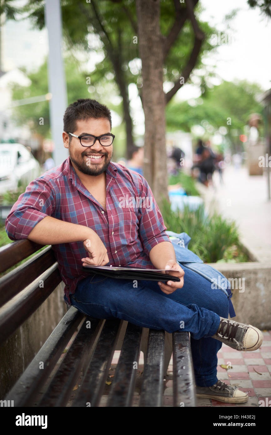 Sorridente ispanico uomo seduto su un banco di lavoro leggendo la brochure Foto Stock