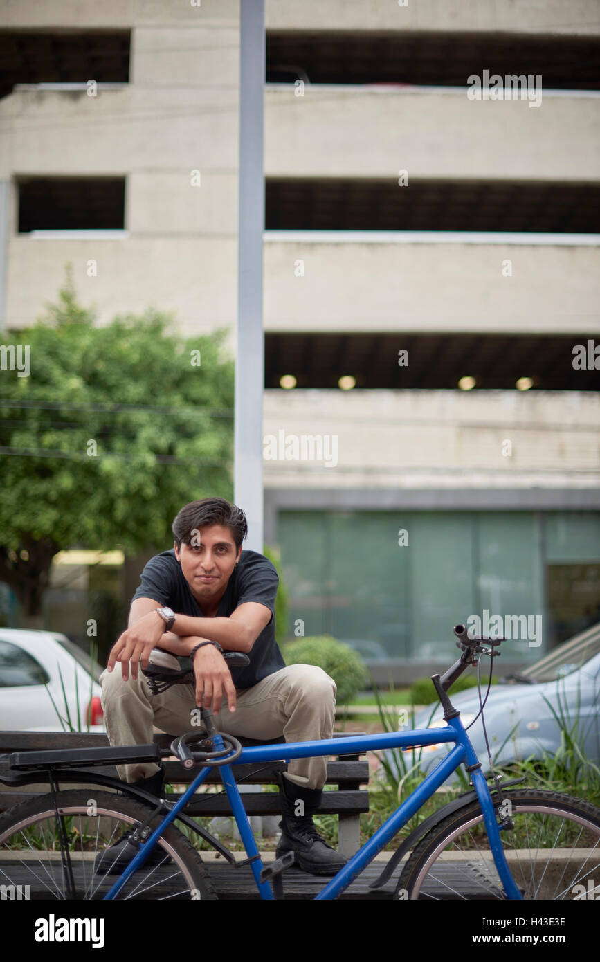 Sorridente ispanico uomo seduto su un banco di lavoro con la bicicletta Foto Stock
