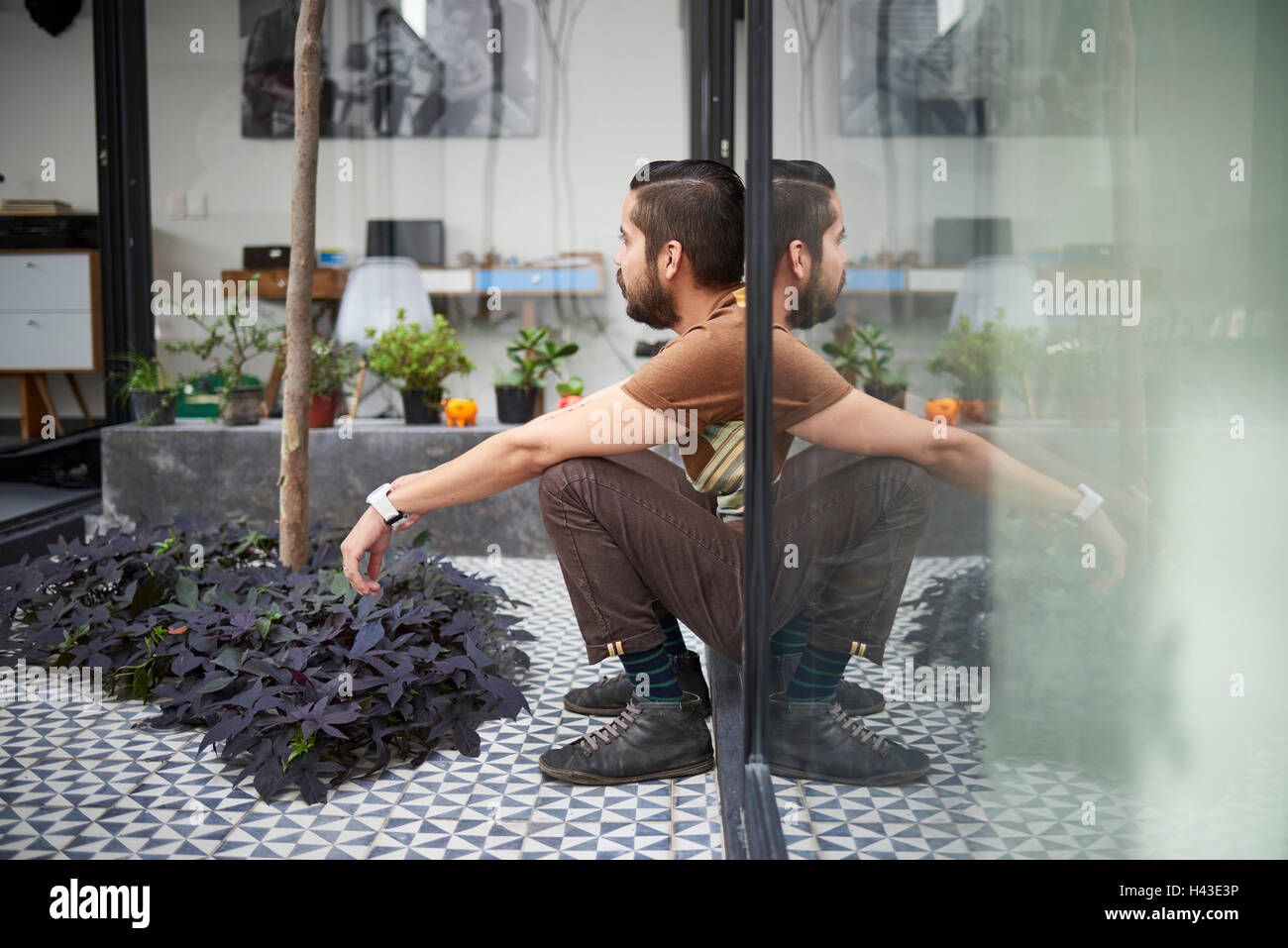 La riflessione di seduta uomo ispanico nella finestra atrio Foto Stock
