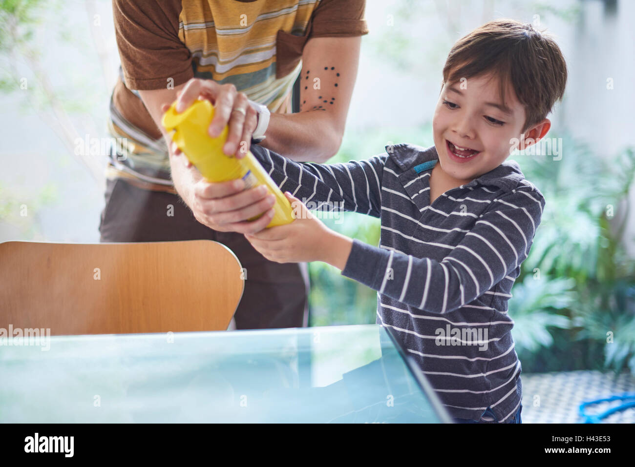 Ragazzo ispanico aiutando padre spruzzare il detergente sul tavolo Foto Stock