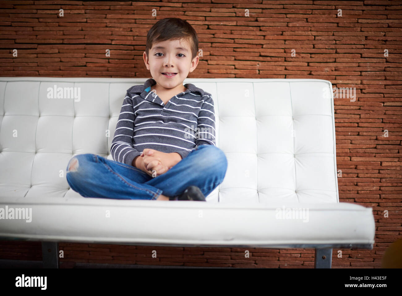 Ispanico ragazzo seduto a gambe incrociate sul divano Foto Stock