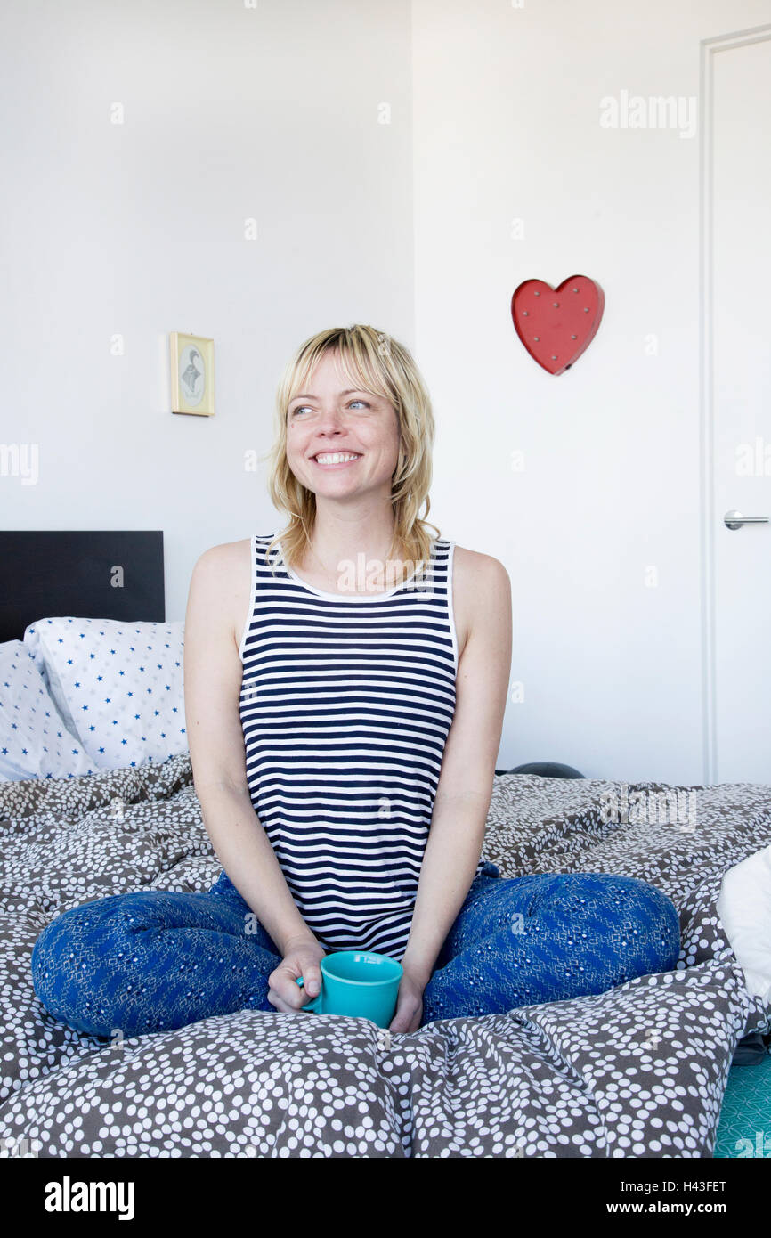 Caucasian donna seduta sul letto di bere il caffè Foto Stock
