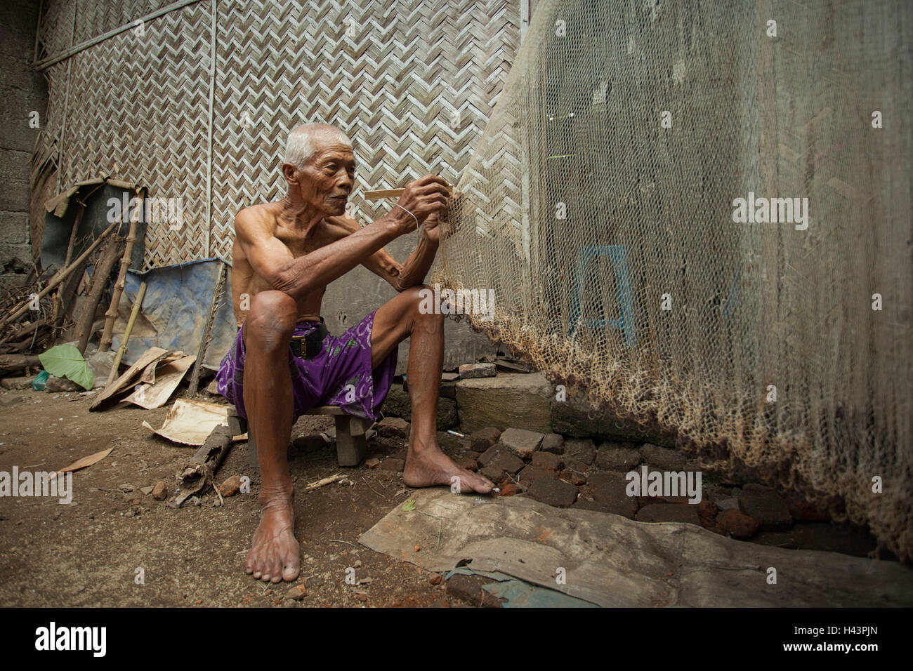 Senior uomo che ripara una rete da pesca, Jember, East Java, Indonesia Foto Stock