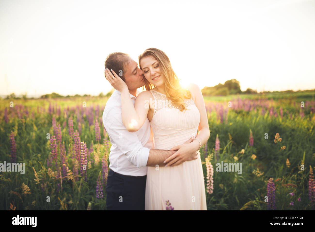 Sposa sposo tiene il collo mentre lui le bacia il sotto i raggi del sole al tramonto Foto Stock
