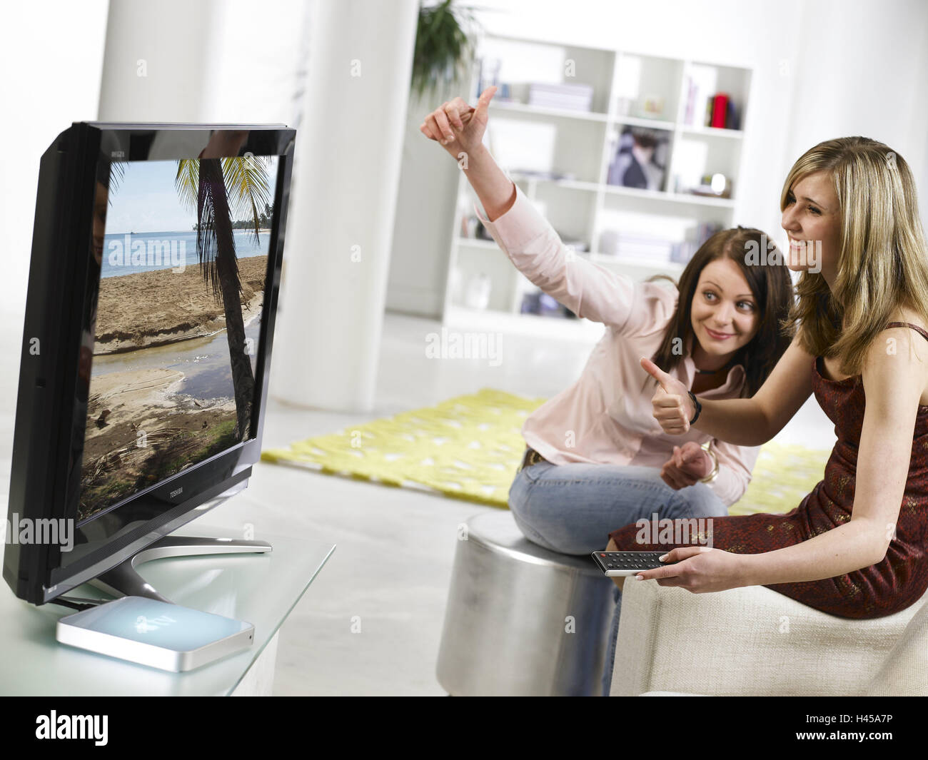 Camere salotto, ragazze, guarda la TV, passare Apple TV, felice, gesto, positivamente, tempo libero e attività per il tempo libero, Elettronica di consumo, TV, TV a schermo piatto LCD TV, Apple TV, intrattenimento, possibilità, la riproduzione di musica, video, podcast, TV, caricamenti di foto, persone, sorelle, amici, insieme, telecomando, set top altoparlante, all'interno, Foto Stock