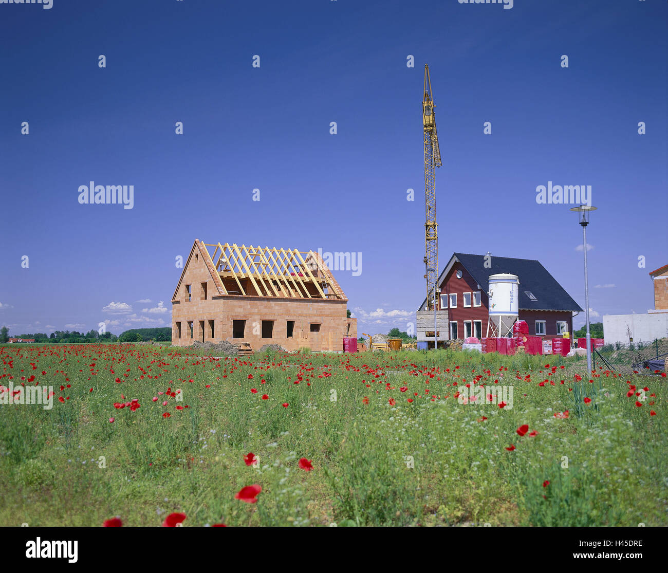 In Germania, in Baviera, la costruzione di una casa, abitazioni unifamiliari, semi di papavero campo, case, costruire muri di fondazione, travi del tetto, capriata, mattoni rossi, ponteggi, cemento silo, casa di nuova costruzione, settore immobiliare, casa, deserte, fuori casa residenziale, la proprietà di risparmio di costruzione, costruzione gru, gru, lanterna, area building, scenario, shell, cielo, prato, fiori, semi di papavero, sviluppo di alloggiamento, la nuova area di costruzione, Foto Stock