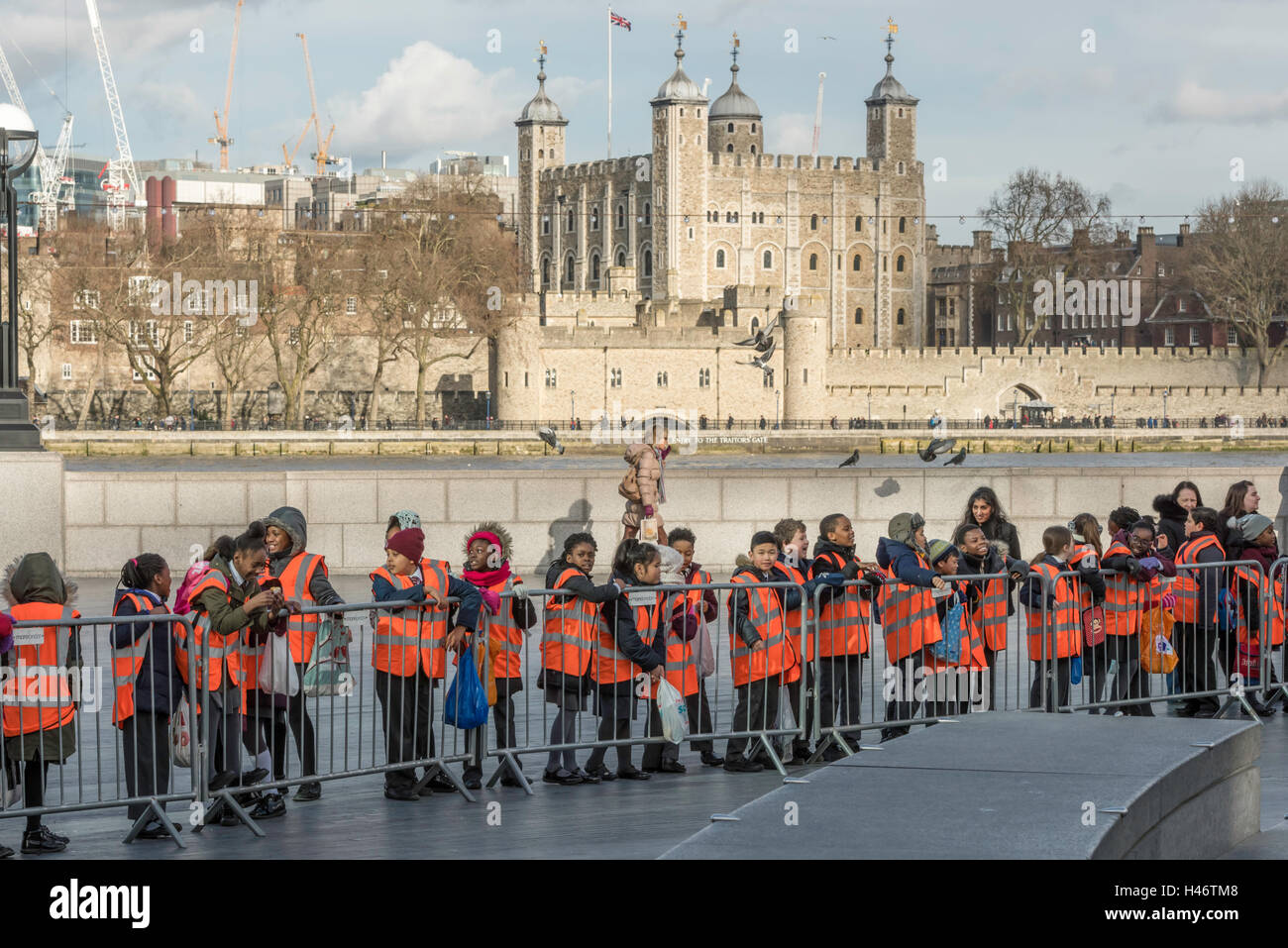 Un gruppo di giovani la scuola dei bambini in uniforme e di alta visibilità arancione giacche in un giorno di viaggio in piedi lungo il Tamigi, di fronte alla Torre di Londra. Foto Stock