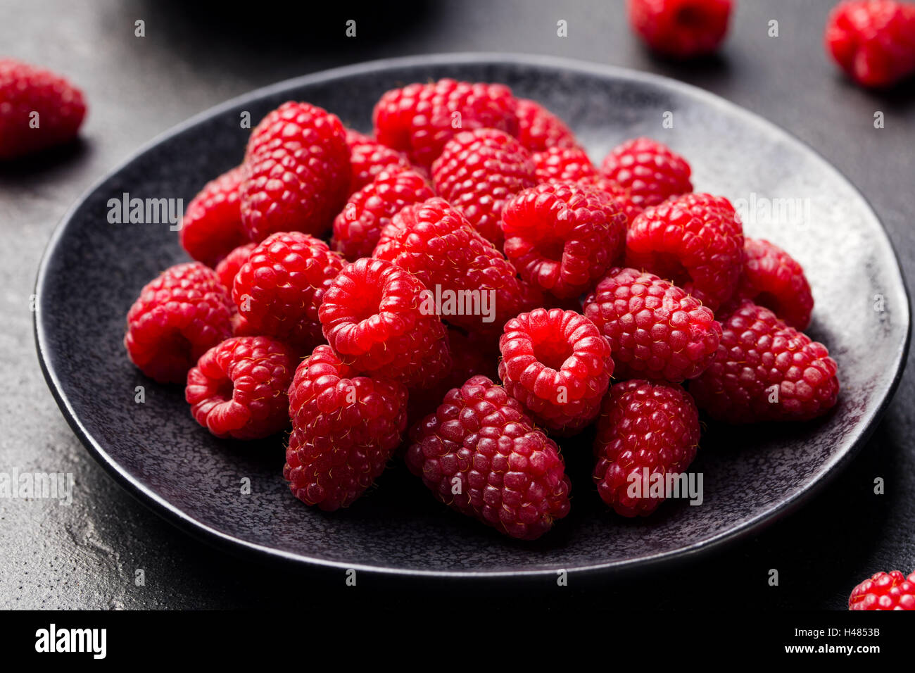 Lamponi freschi su una ciotola nero lo sfondo di pietra Foto Stock