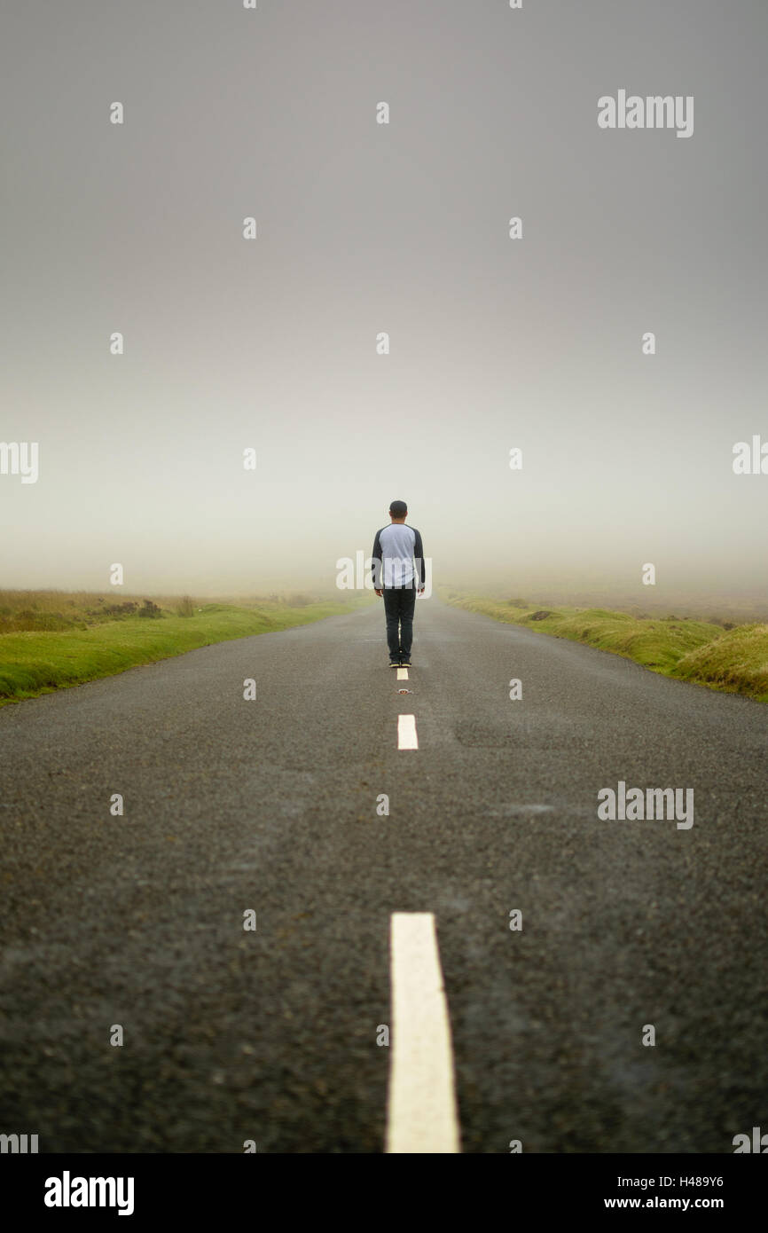 L uomo si erge nel mezzo di un vuoto di strada in Dartmoor, Inghilterra Foto Stock