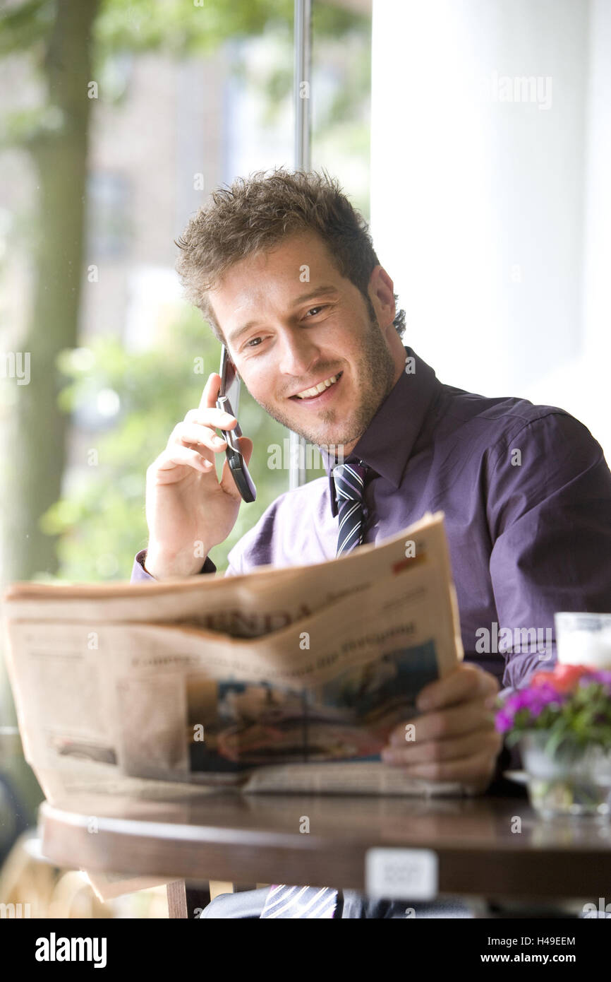 Cafe, uomo giovane, allegro, giornale, leggere, richiamare, il telefono cellulare e il sorriso, ritratto, gastronomia, bar, bistro, tempo libero, pausa pranzo, pausa, pausa di lavoro, valutazione, business, imprenditore, persona, barba di tre giorni, barba lunga, smart, sit sit, allegramente, giornale, telefono, news, felice, contently, chiamata, telefono cellulare, di comunicazione, di telecomunicazione, svago, divertimento, mobilità, all'interno, Foto Stock