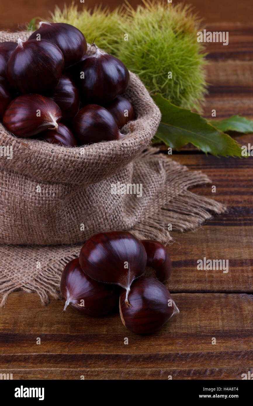 Le castagne fresche nel sacco di tela su sfondo rustico, spazio di copia Foto Stock