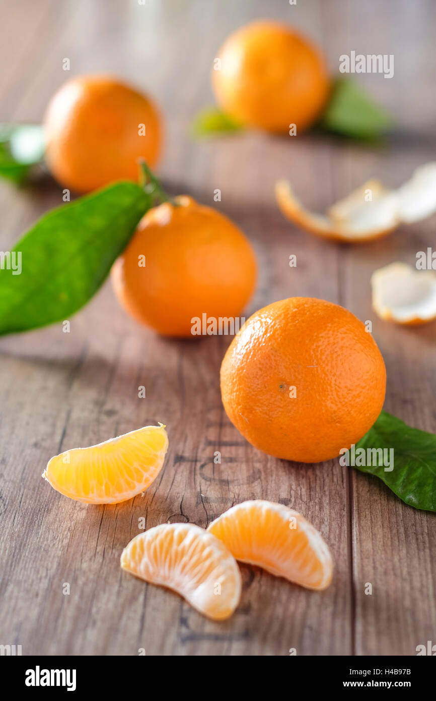 Clementine con fogliame, pezzi di clementine e sbucciate su un tavolo di legno Foto Stock