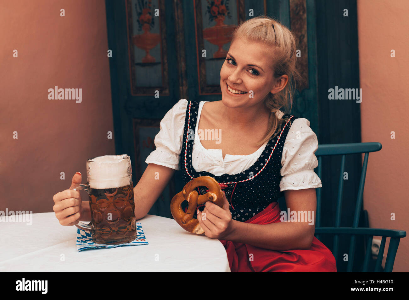 Donna seduta al tavolo con boccale di birra e pretzel Foto Stock