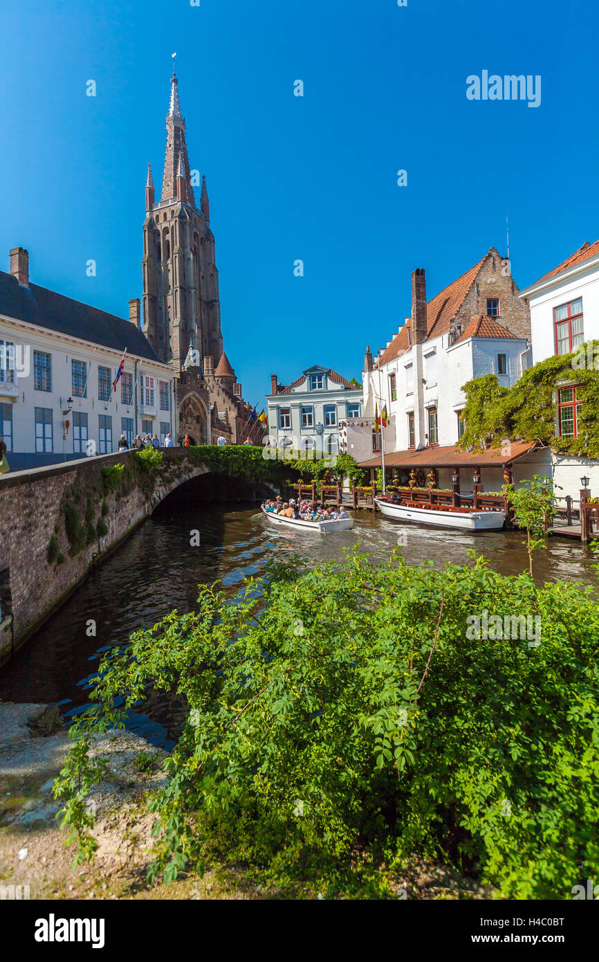 BRUGES, Belgio - Aprile 6, 2008: turisti galleggiare su una barca attraverso il canale vicino Dijver ponte e la chiesa di Nostra Signora Foto Stock