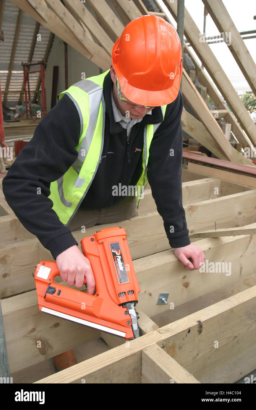 Un builder utilizza un gas-powered pistola sparachiodi per fissare il legname di supporti antisismici tra pavimento travetti su una casa in fase di ristrutturazione Foto Stock